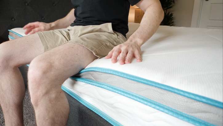 A man sits on the edge of a hybrid mattress.