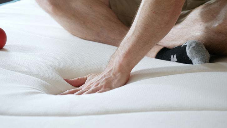 A man presses his hand into a mattress.